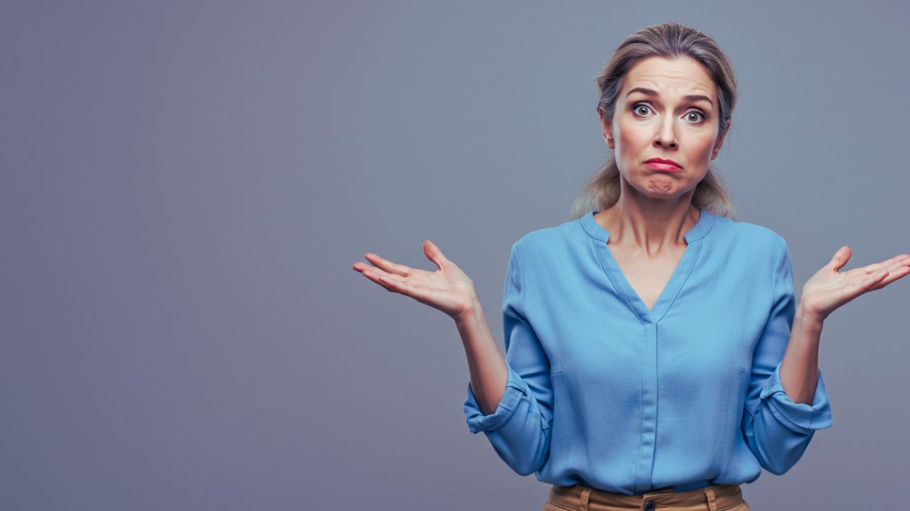 A confused woman shrugging with her palms up, looking directly at the camera with a questioning expression.