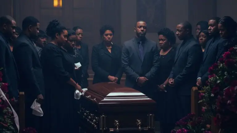 A group of people dressed in black stands solemnly around a closed casket at a funeral service, expressing grief.
